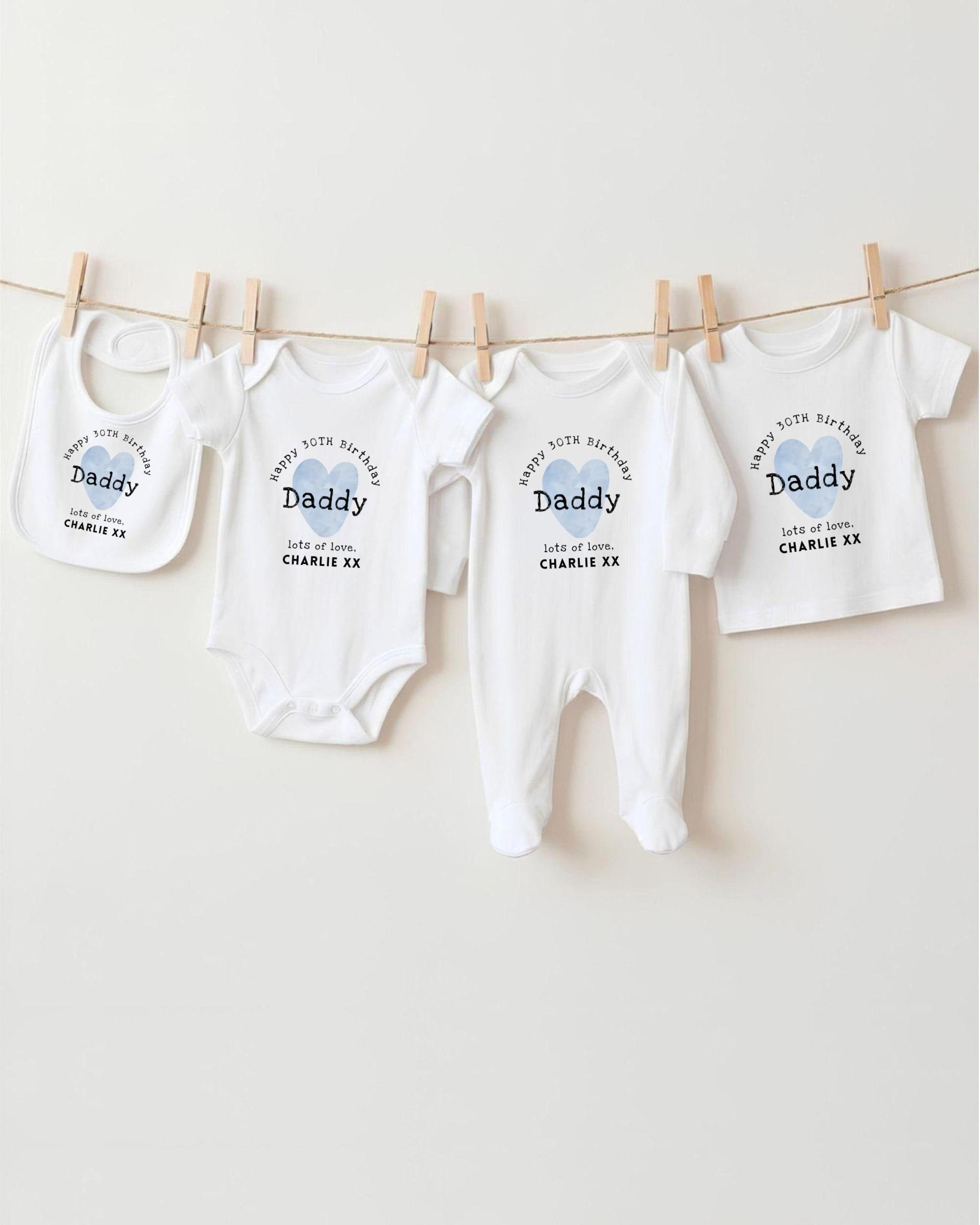 A row of white baby clothes, including onesies and bibs, hanging on a clothesline.