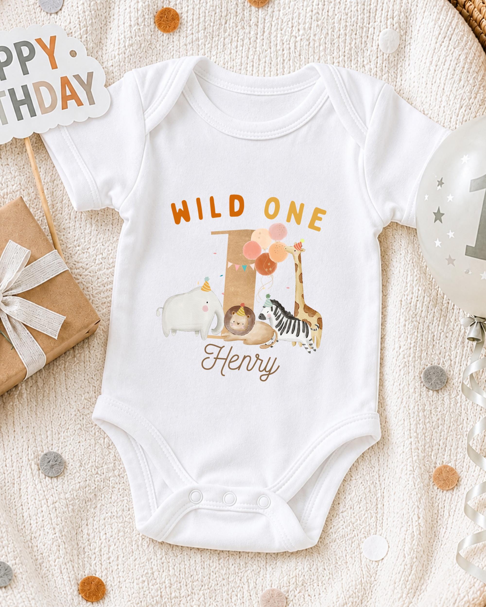 A white onesie with a wild animal design and the text "Wild One Henry" printed on it, along with a birthday sign and a balloon.