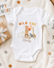 A white onesie with a wild animal design and the text "Wild One Henry" printed on it, along with a birthday sign and a balloon.