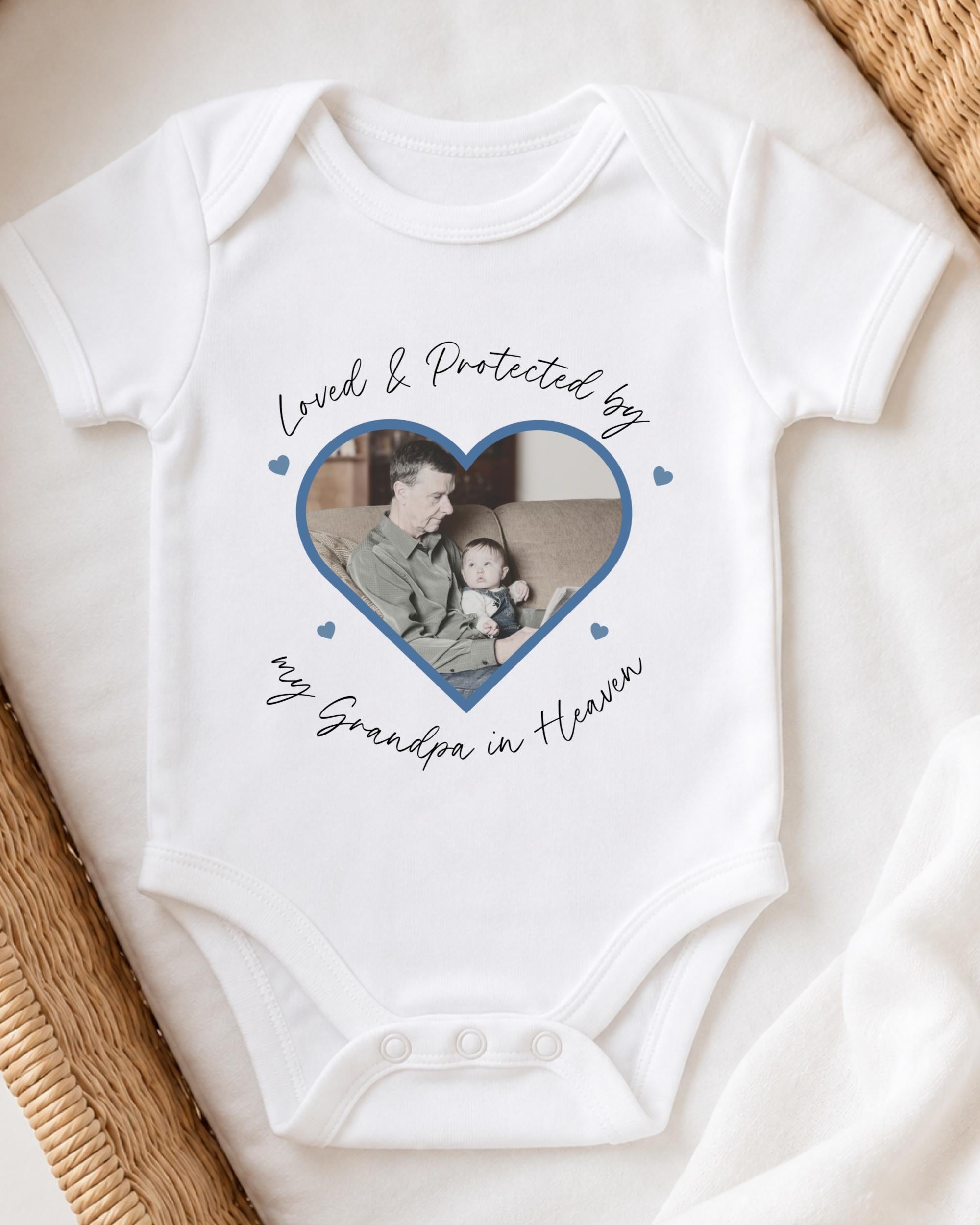 A white baby onesie with a heart-shaped photo of a man and a child, along with the text "Loved & Protected by my Grandpa in Heaven" printed on it.