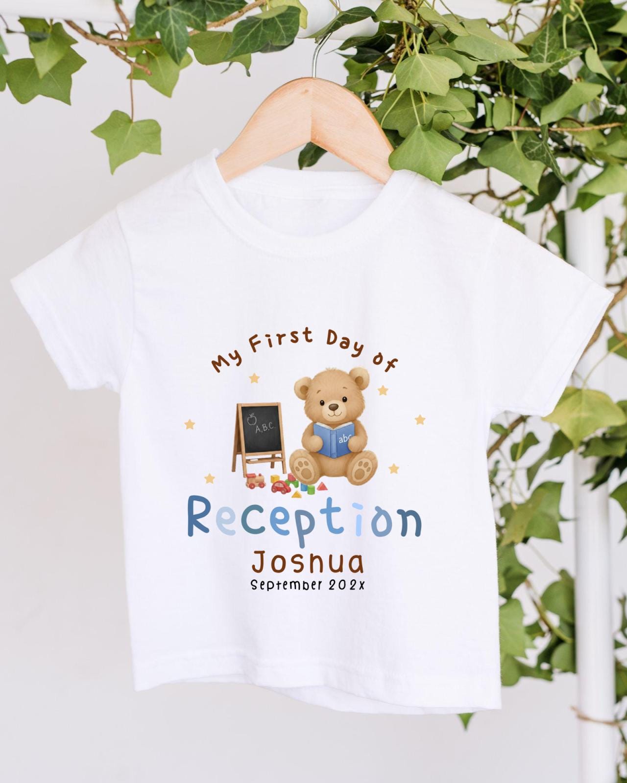 A white t-shirt with a teddy bear and a chalkboard, along with the text "My First Day of Reception Joshua September 2023".