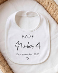 A white baby bib with the text "BABY Number 4 Due November 2025" printed on it.