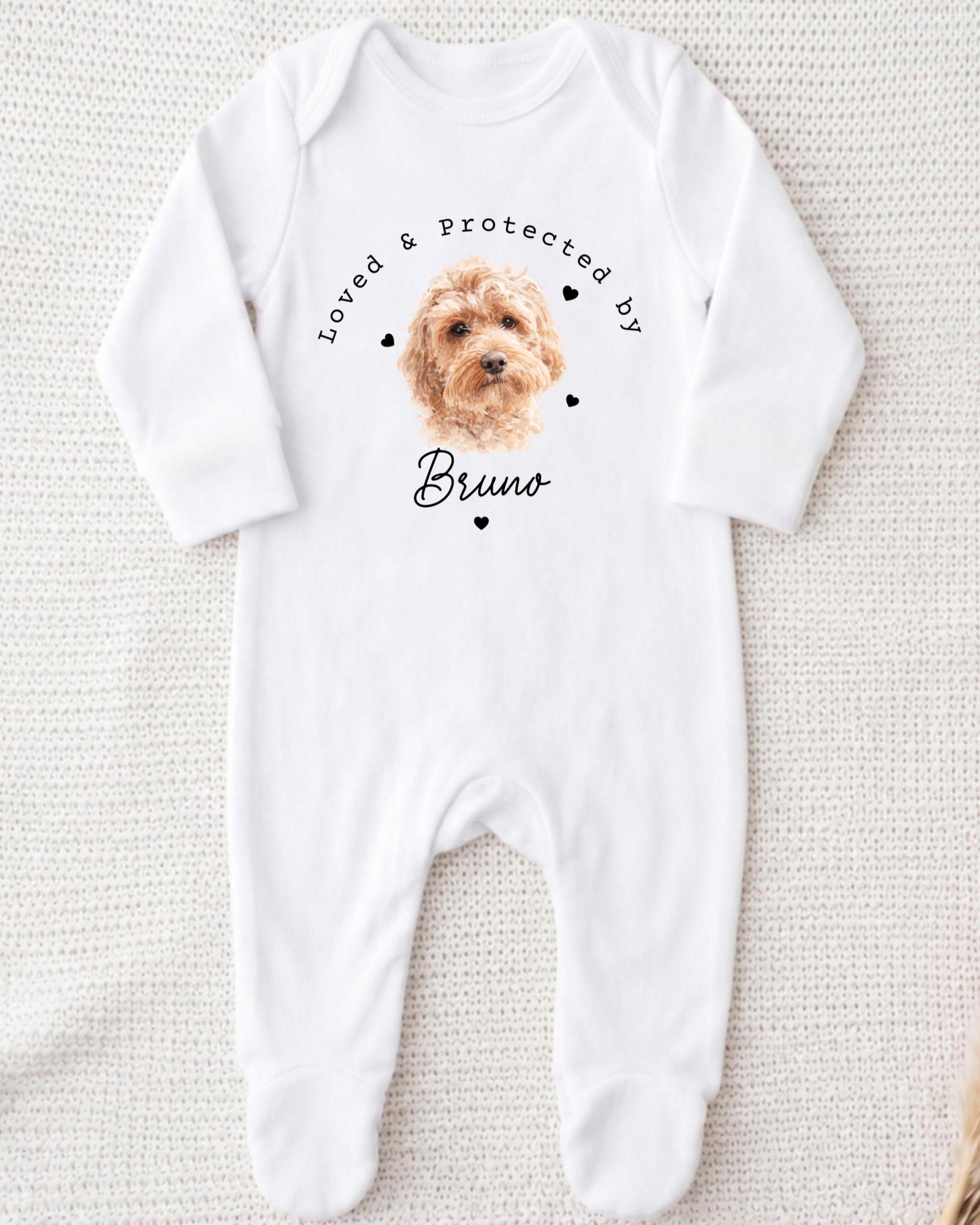 A white onesie with a printed image of a dog and the text "Loved & protected by Bruno" printed on it.