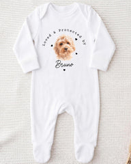 A white onesie with a printed image of a dog and the text "Loved & protected by Bruno" printed on it.