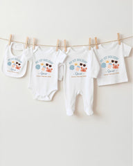 A row of four white baby clothes, including onesies and pajamas, hanging on a clothesline.