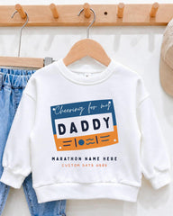 A white sweatshirt with a graphic design that says "Cheering for my DADDY" and "MARCHON NAME HERE" printed on it, hanging on a wooden hanger.