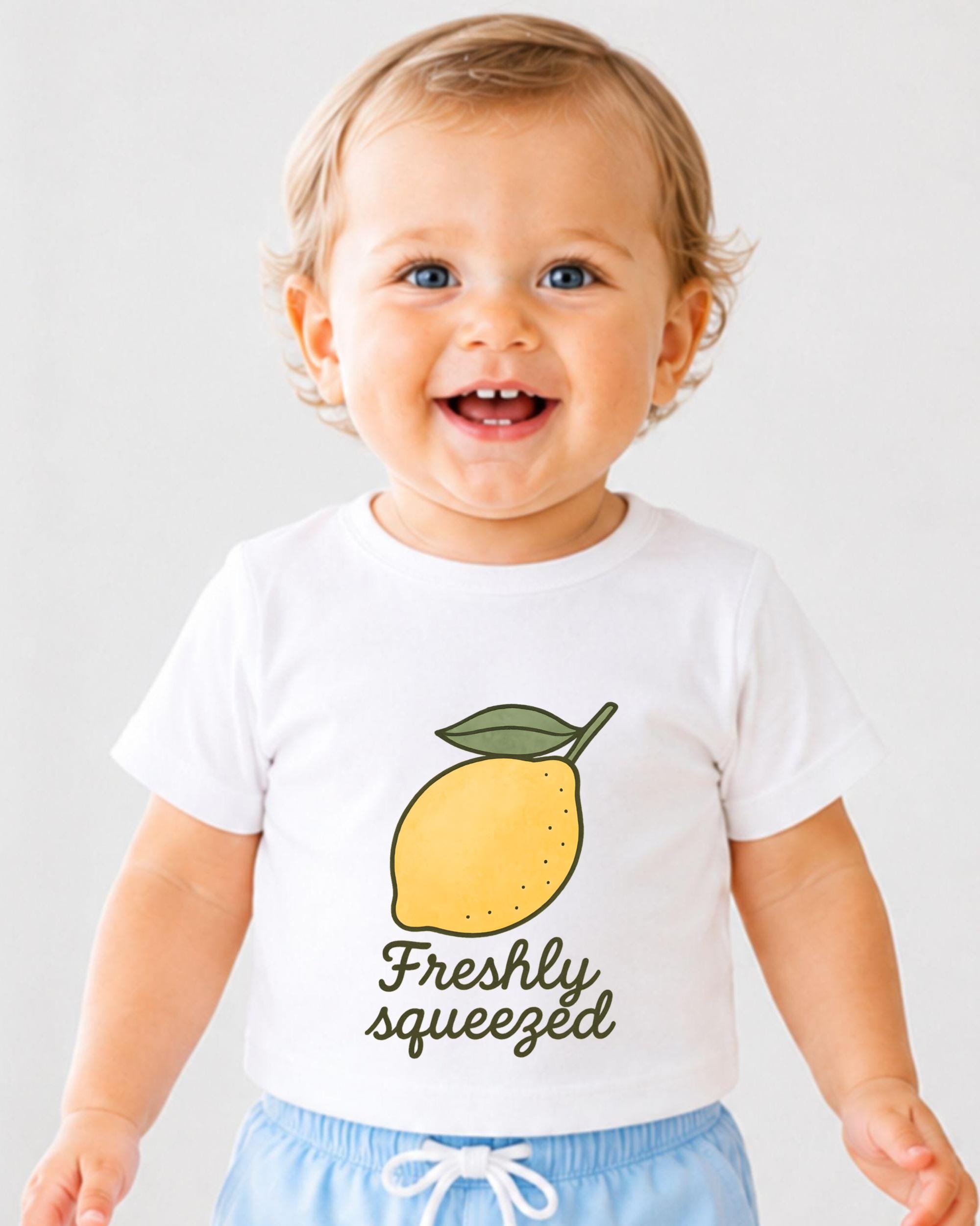 A smiling baby wearing a white t-shirt with a lemon graphic and the text "Freshly squeezed" printed on it.