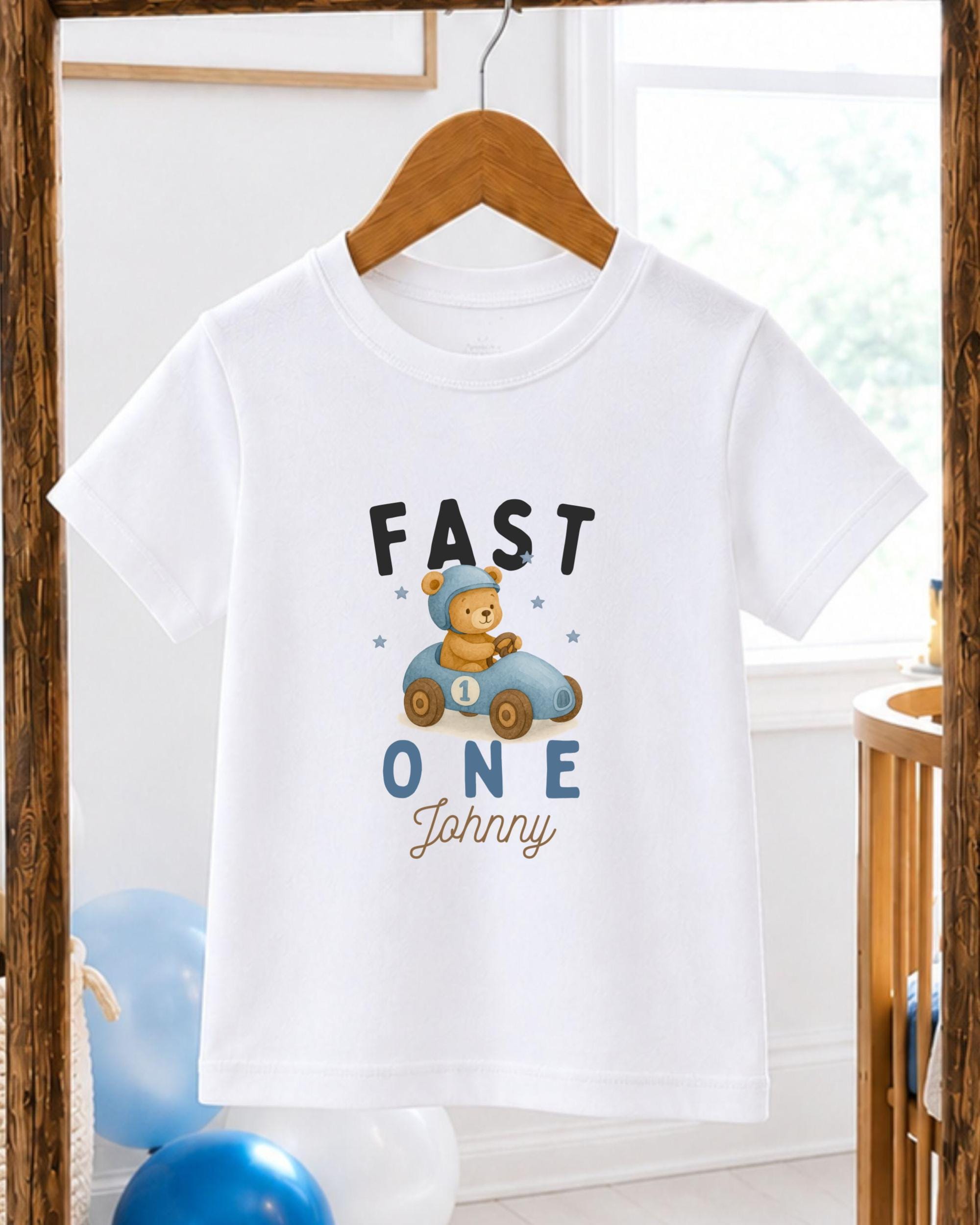 A white t-shirt with a cartoon image of a teddy bear in a race car and the text "FAST 1 Johnny" printed on it.