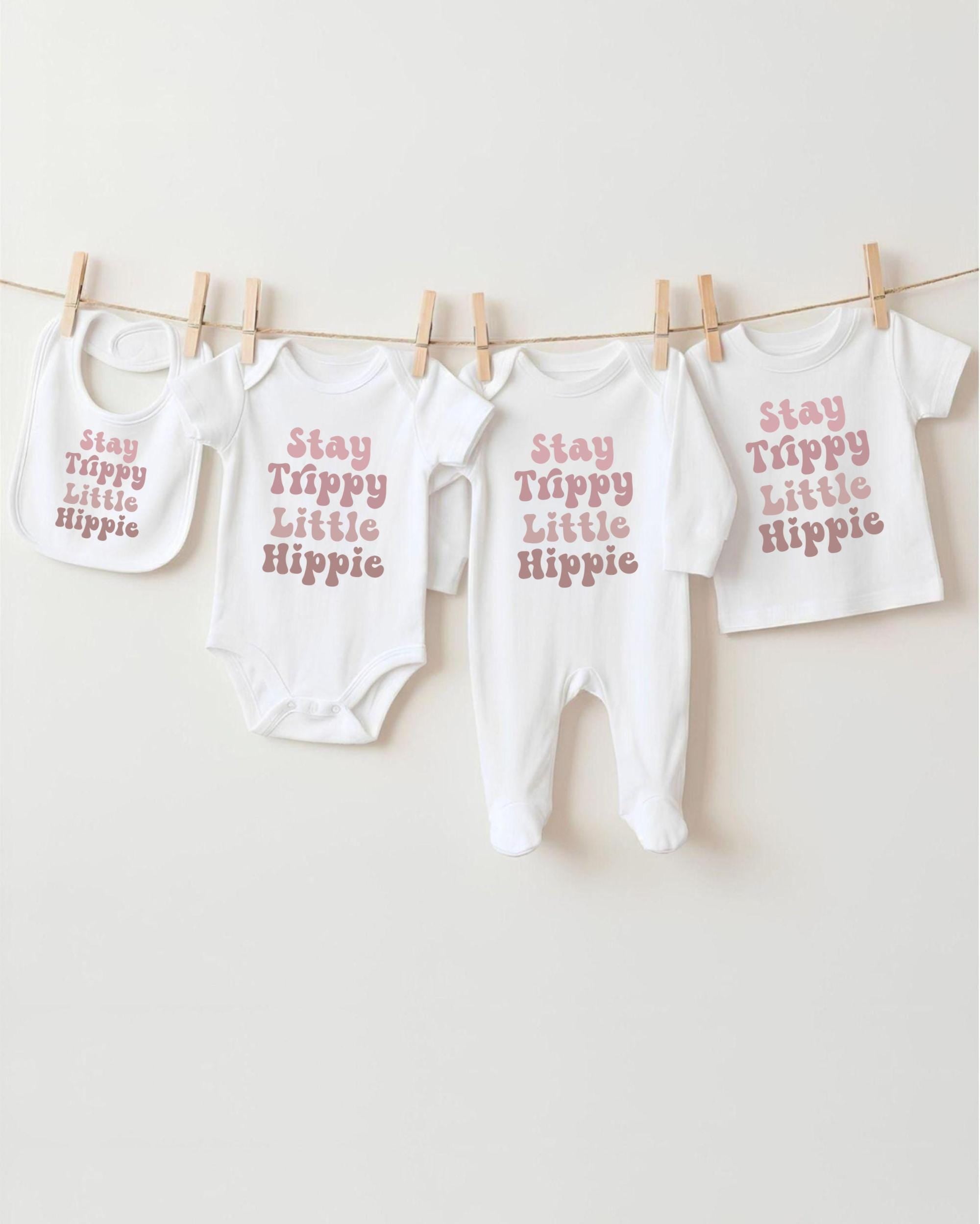 A collection of baby clothes, including onesies and bibs, hanging on a clothesline.