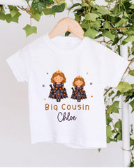 A white t-shirt with a graphic design featuring two cartoon princesses wearing crowns, surrounded by stars and text that reads "Big Cousin Chloe".