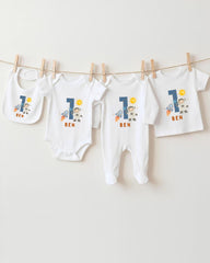 A collection of white baby clothes, including onesies and bibs, with the name "Ben" printed on them. The clothes are hanging on a clothesline, and there are four of them in total.