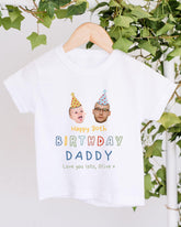 A white t-shirt with a birthday message and two cartoon images of a man and a baby wearing party hats.