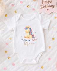 A white onesie with a unicorn graphic and the text "Birthday Girl Sophia" printed on it, surrounded by confetti and a birthday banner.