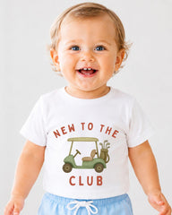A smiling baby wearing a white t-shirt with a golf cart graphic and the text "NEW TO THE CLUB" printed on it.