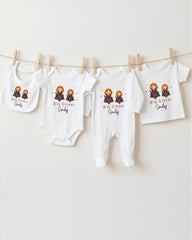 A row of four white baby clothes with the text "Big Sister Emily" printed on them, hanging on a clothesline.