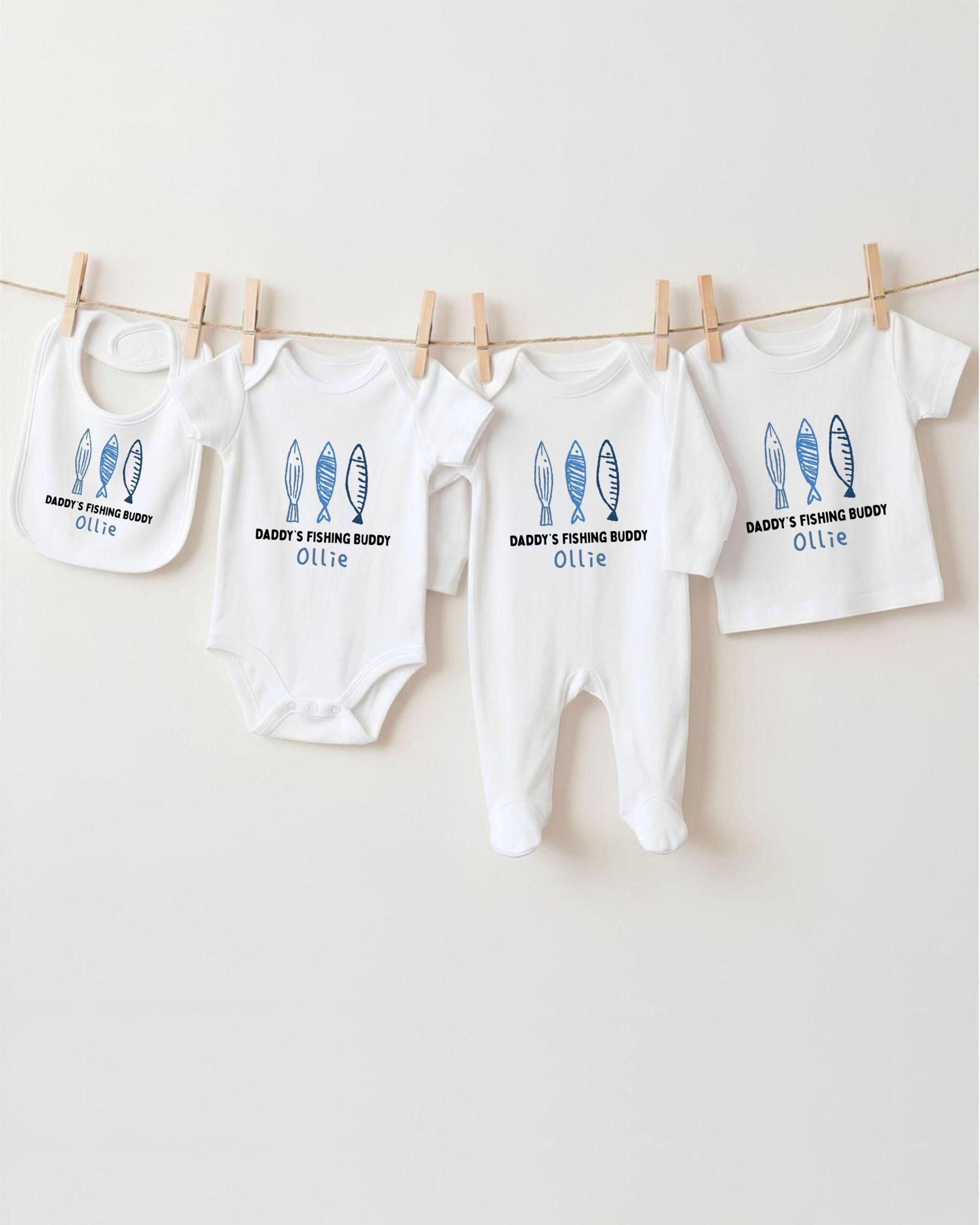 A row of four white baby clothes with blue fish designs, each with a personalized name printed on it, hanging on a clothesline.