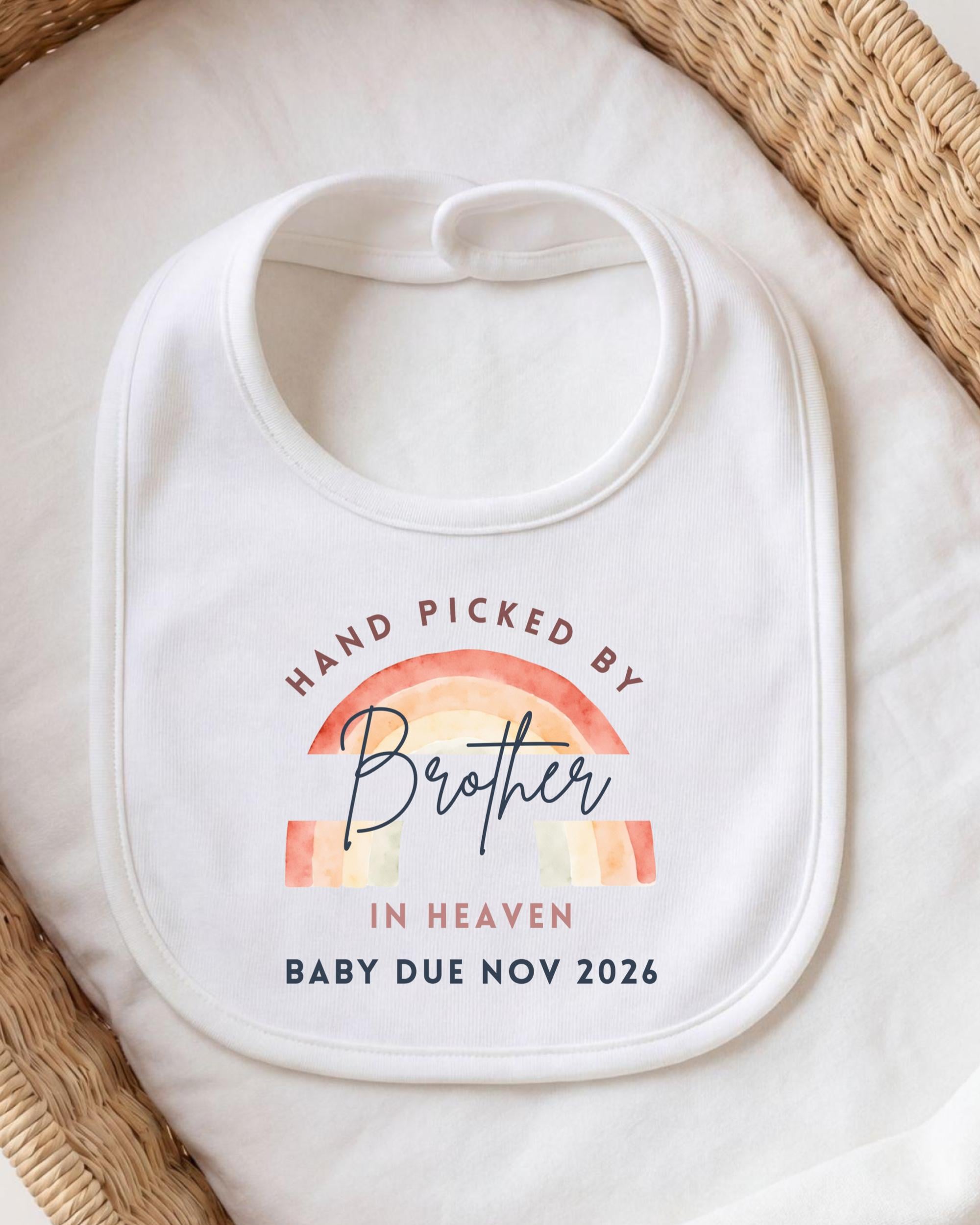 A white baby bib with a printed message that reads "HAND PICKED BY Brother in Heaven BABY DUE NOV 2026".