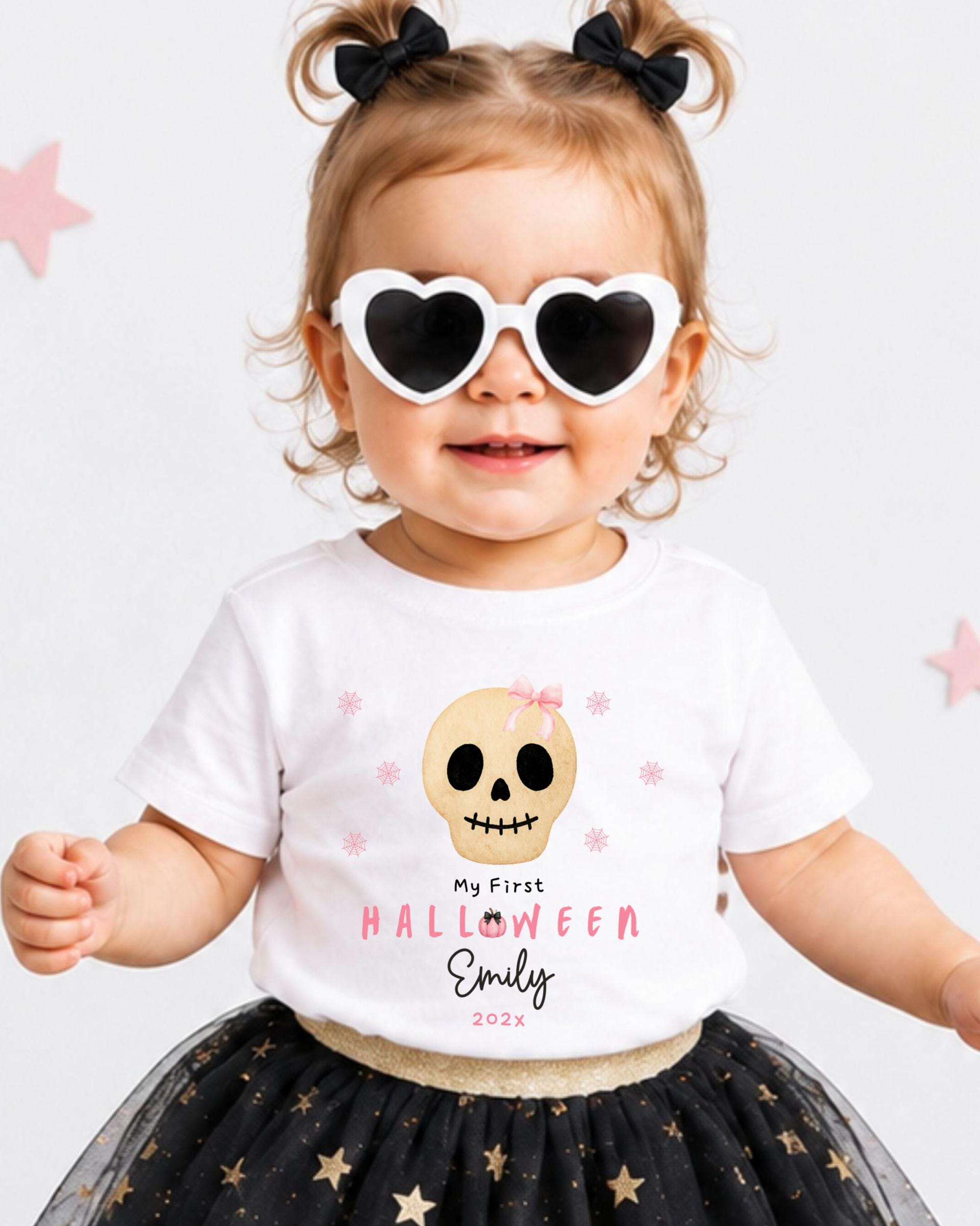 A young girl wearing a white t-shirt with a skull design and heart-shaped sunglasses, smiling and posing for the camera.