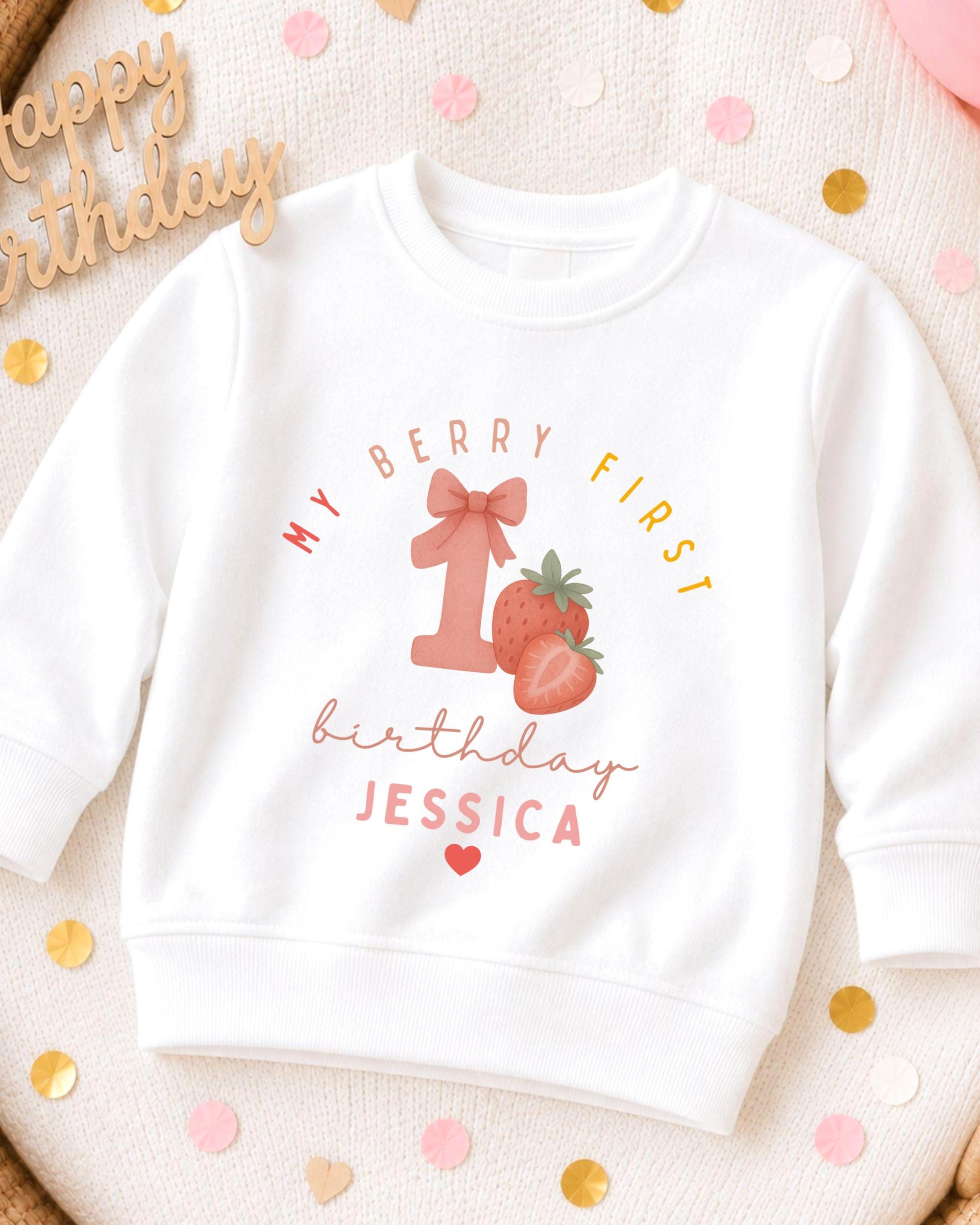 A white sweatshirt with a graphic design featuring a strawberry and the text "My Berry First birthday Jessica" printed on it.