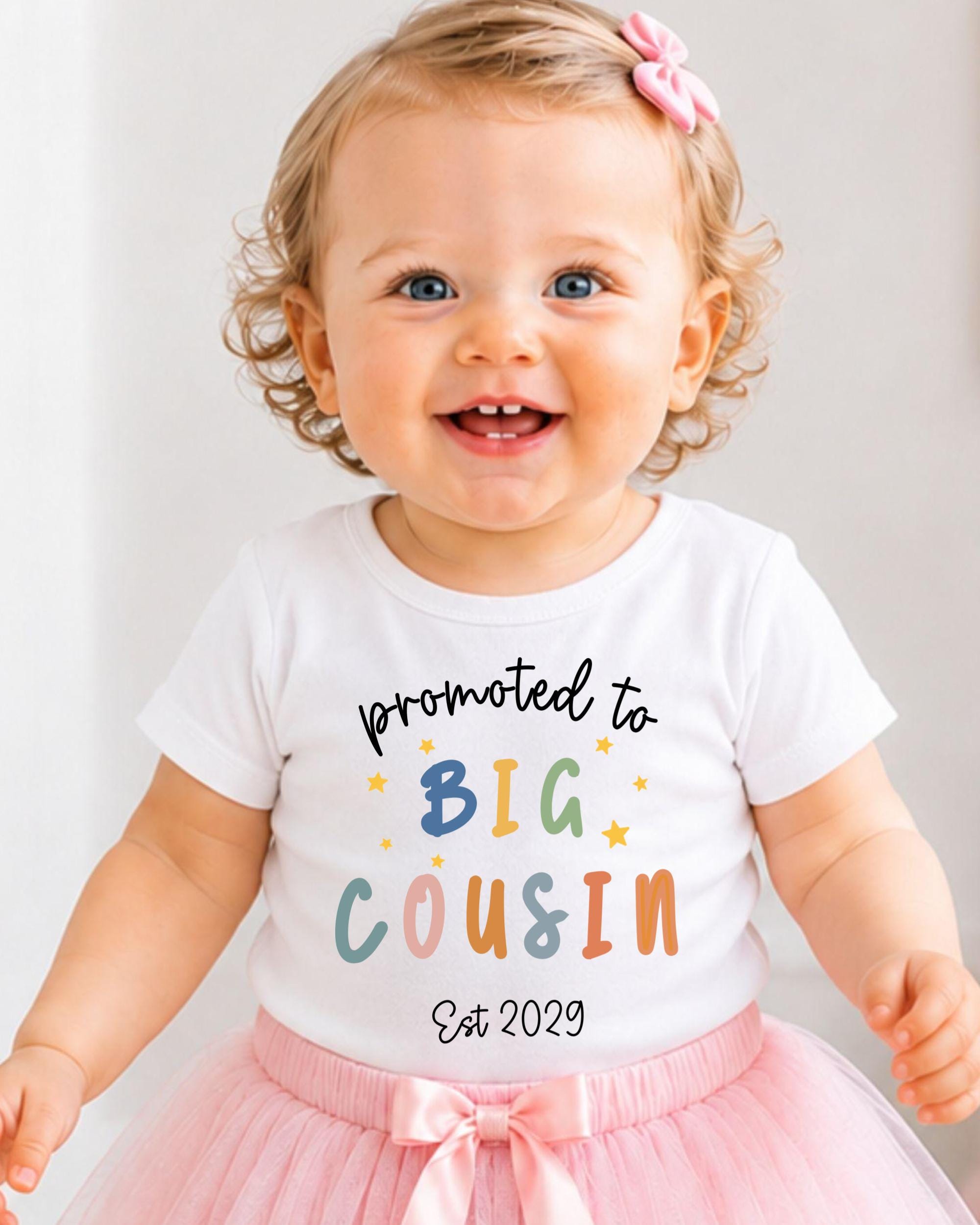 A smiling baby girl wearing a white t-shirt with text and a pink bow.