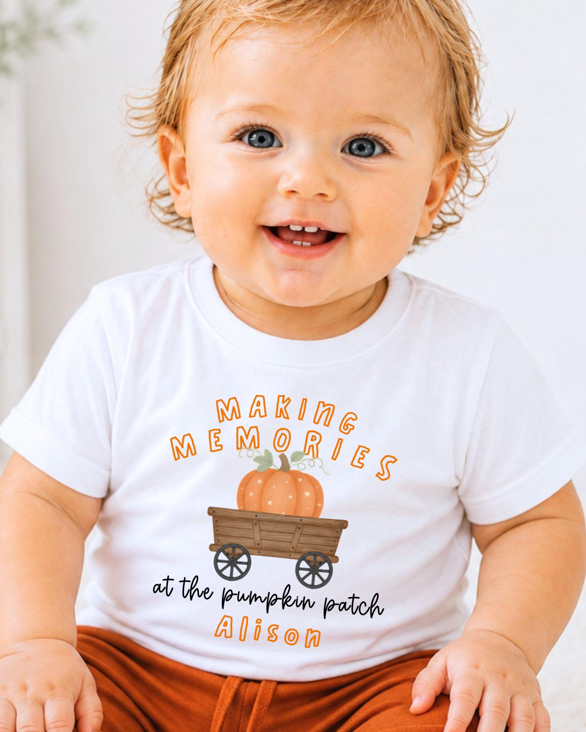 A smiling baby wearing a white t-shirt with a pumpkin patch graphic and text that says "Making memories at the pumpkin patch Alison".