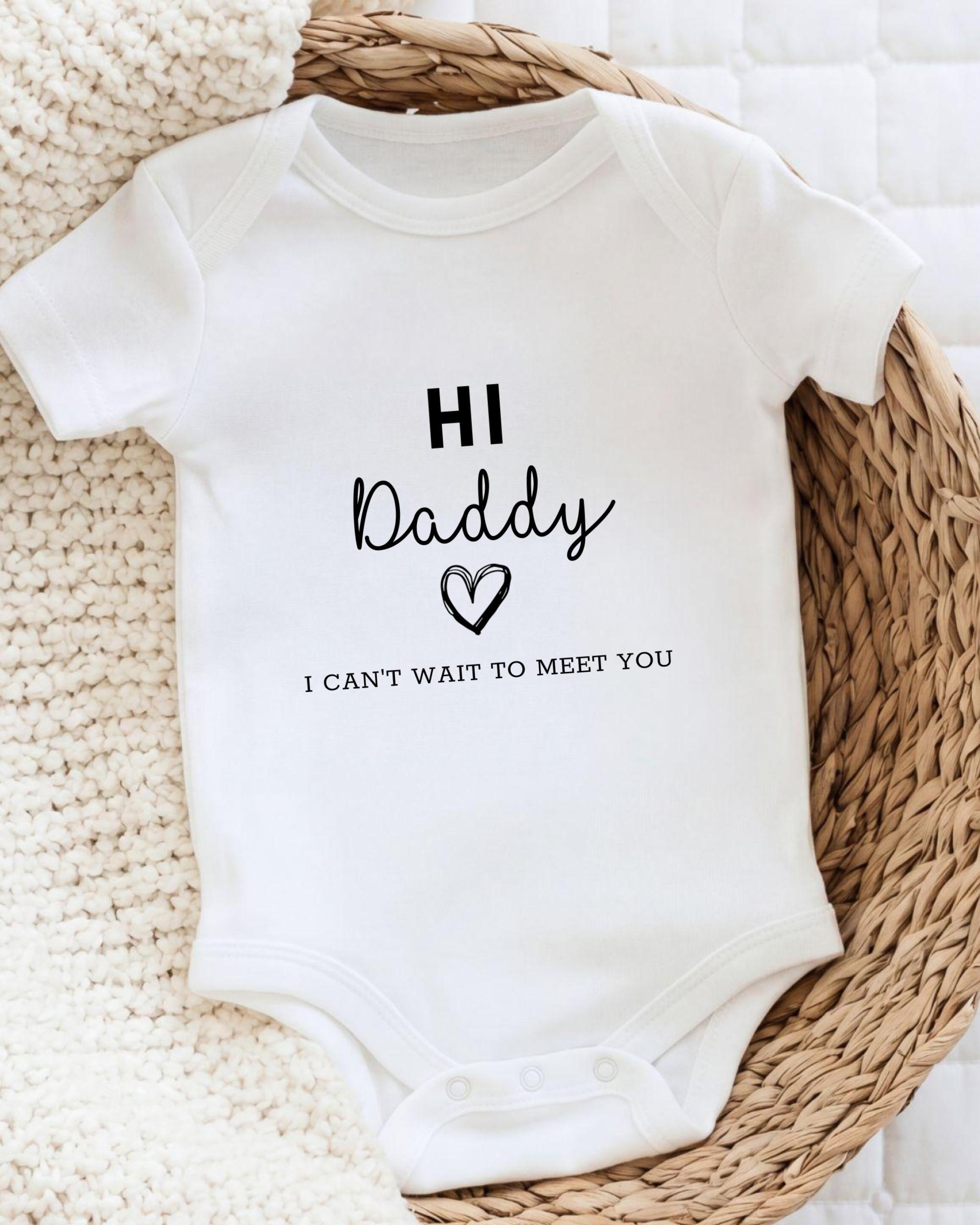 A white baby onesie with the text "HI Daddy I can't wait to meet you" printed on it.