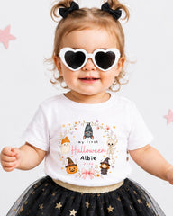 A young girl wearing a white t-shirt with a Halloween-themed design, heart-shaped sunglasses, and a black and gold tutu skirt.