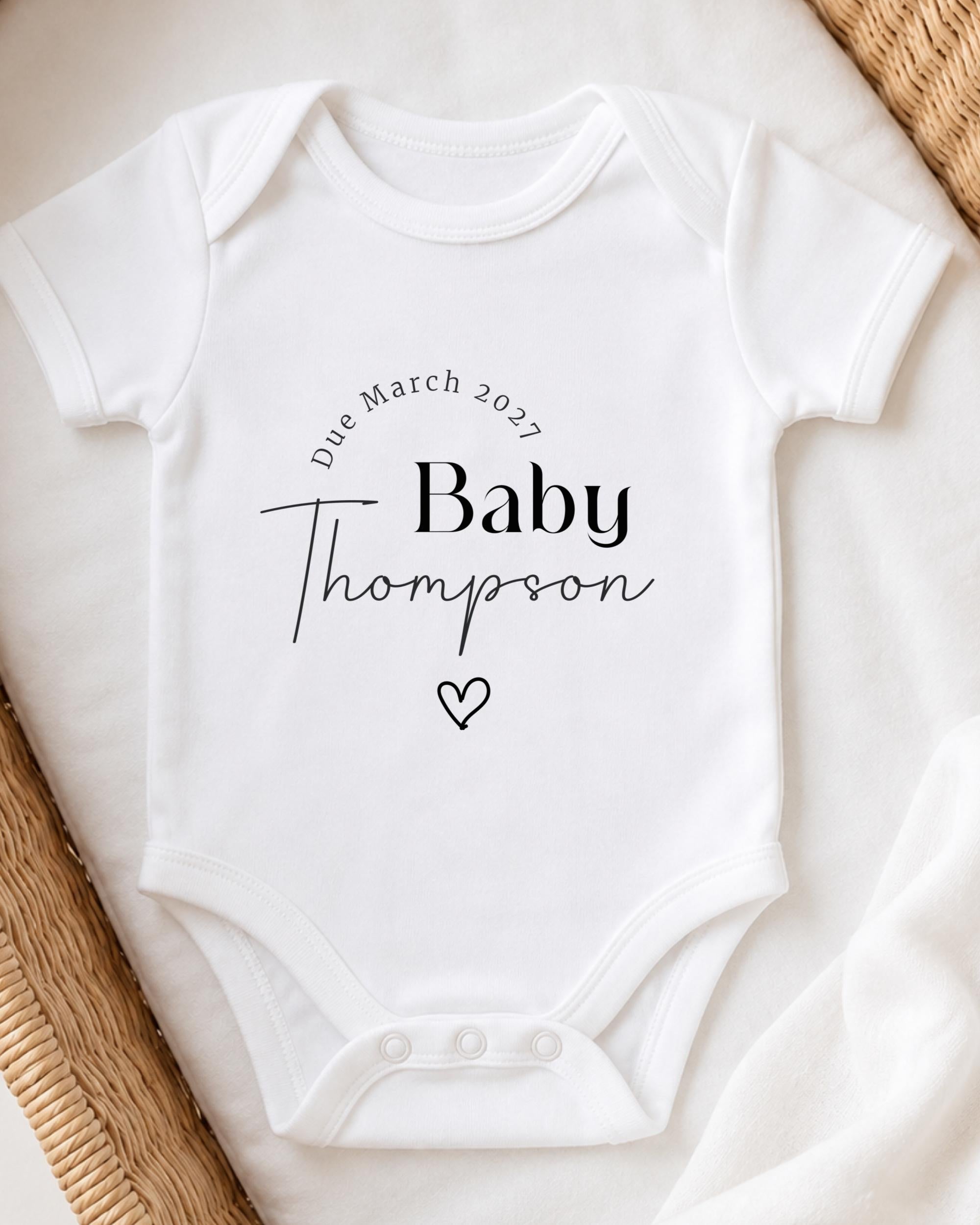 A white baby onesie with the text "Due March 2027 Baby Thompson" printed on it.