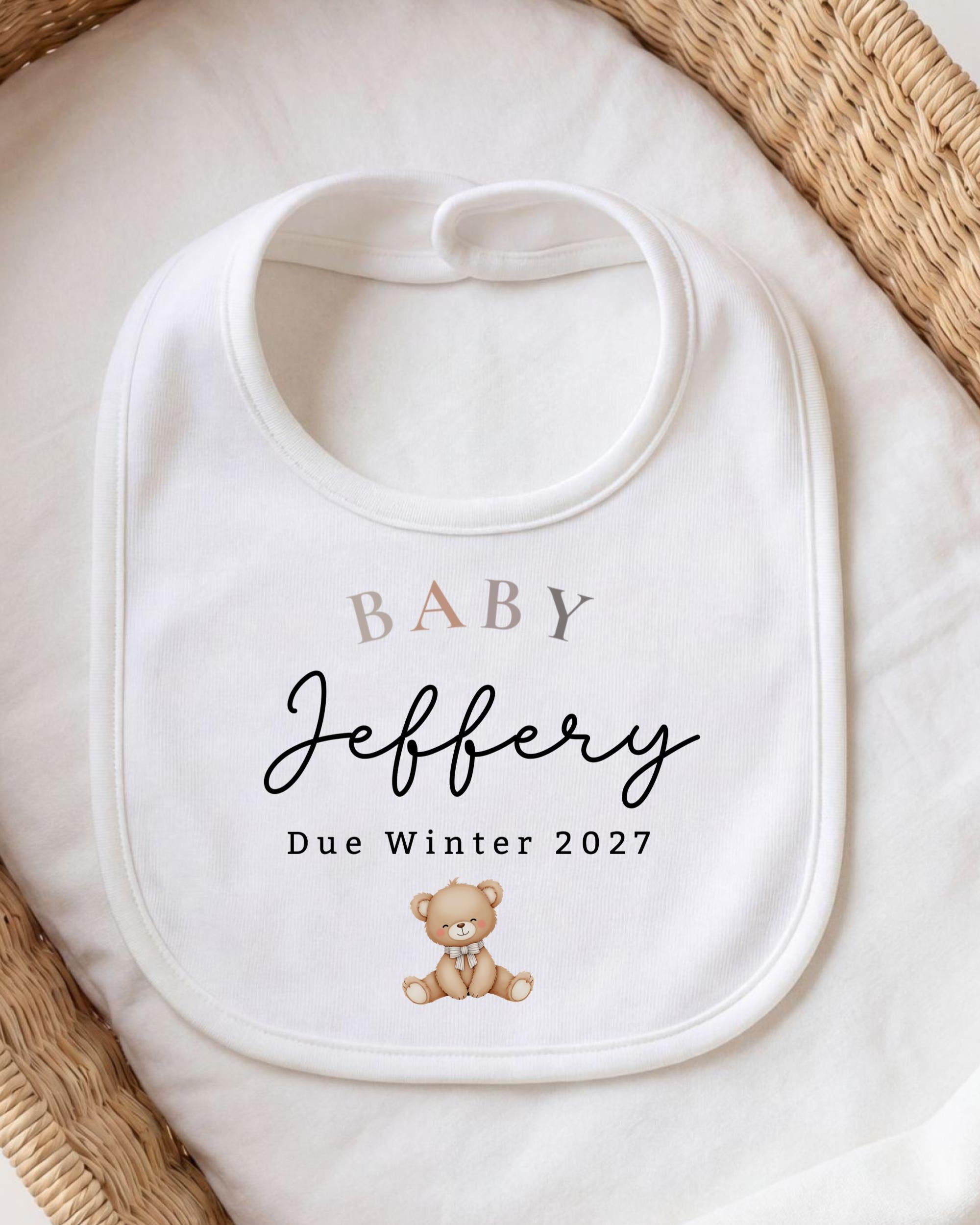 A white baby bib with the name "Jebfery" and the date "Due Winter 2027" printed on it, along with a teddy bear image.