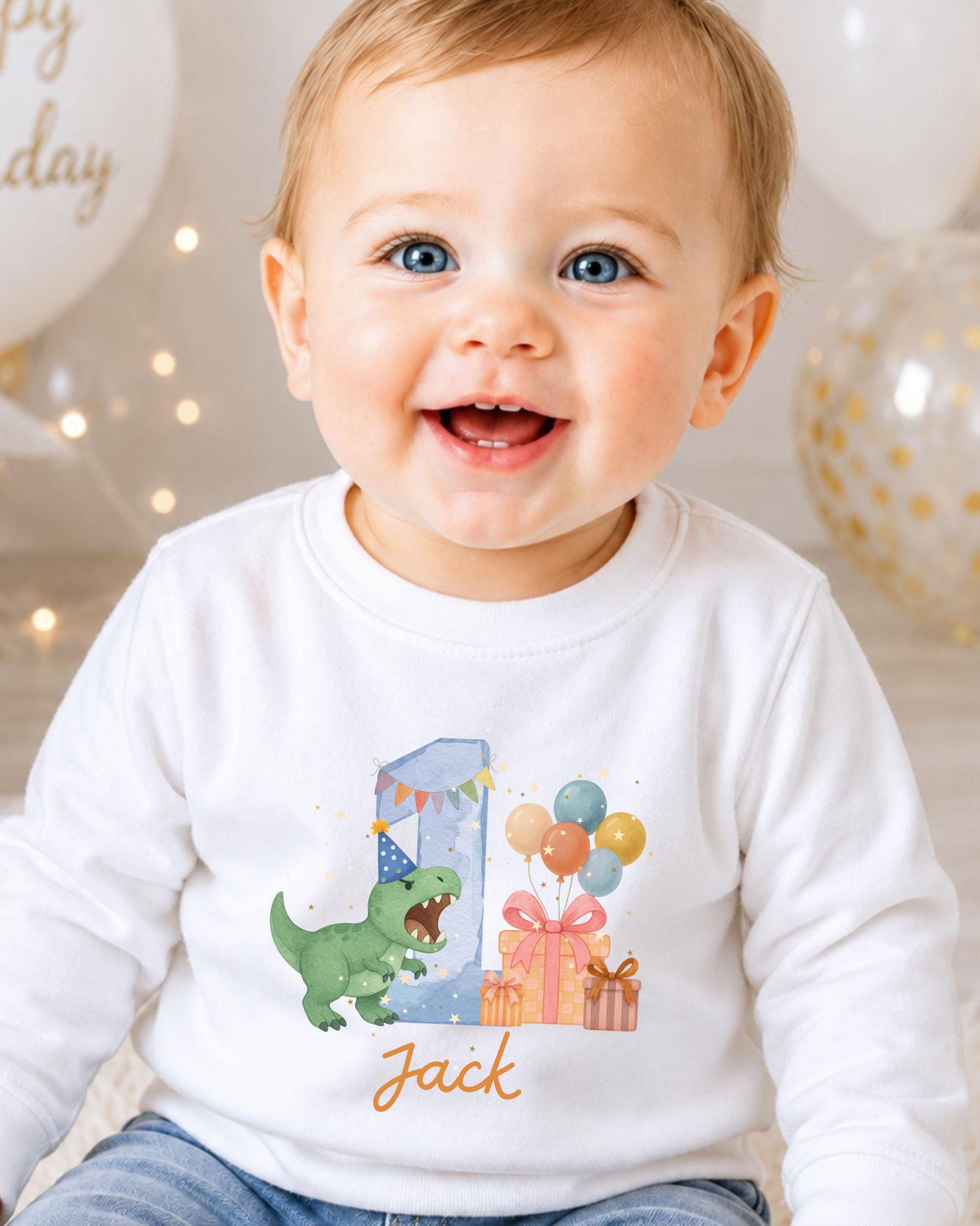 A smiling baby boy wearing a white shirt with a dinosaur and birthday decorations, including balloons and presents.