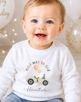 A smiling baby boy wearing a white shirt with a birthday-themed design and the text "Half Way to One Hunter" printed on it.