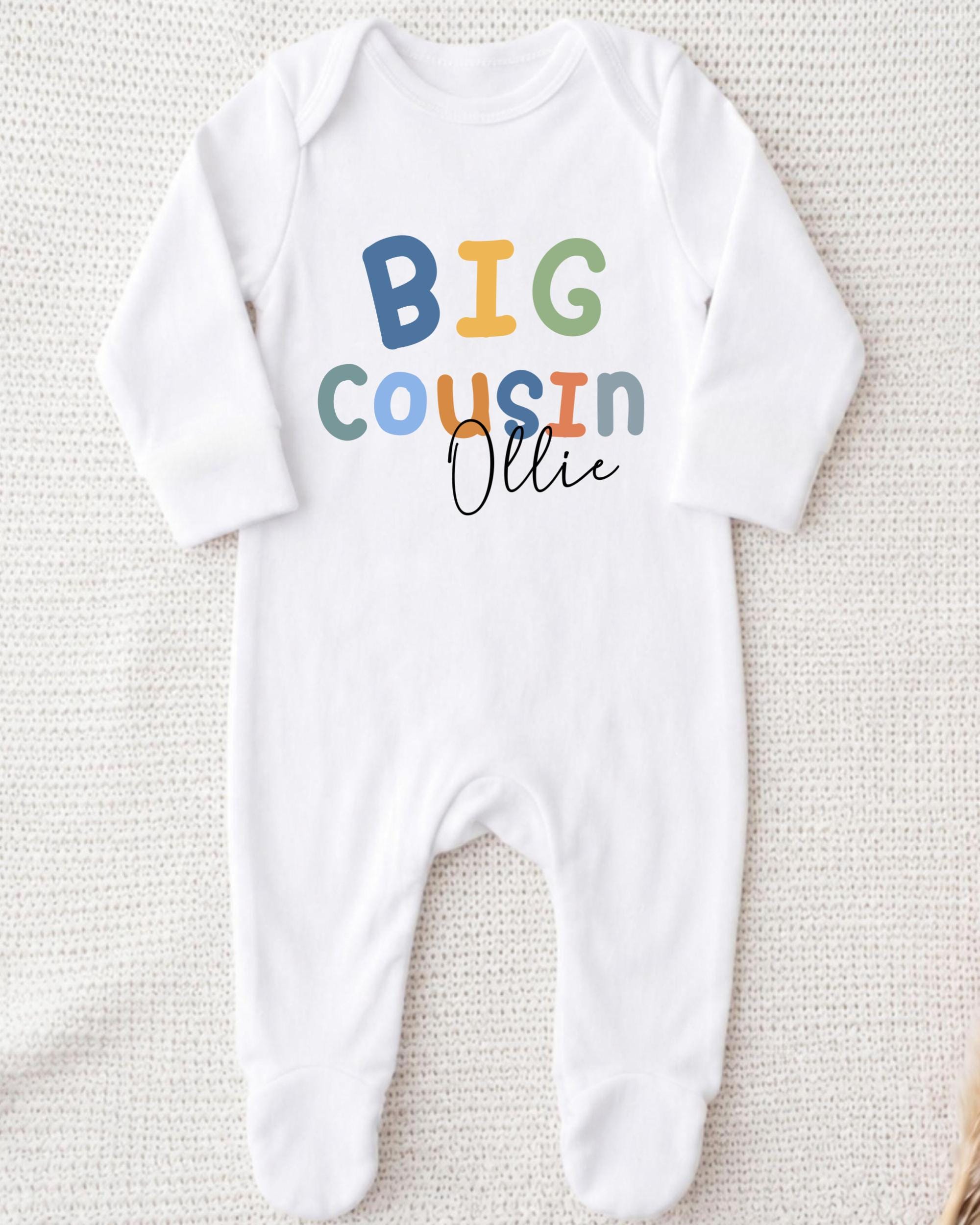 A white onesie with the text "BIG COUSIN OLLIE" printed on it.