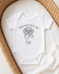 A white baby onesie with a graphic of a dog and the text "PROTECTED BY Bella" printed on it.