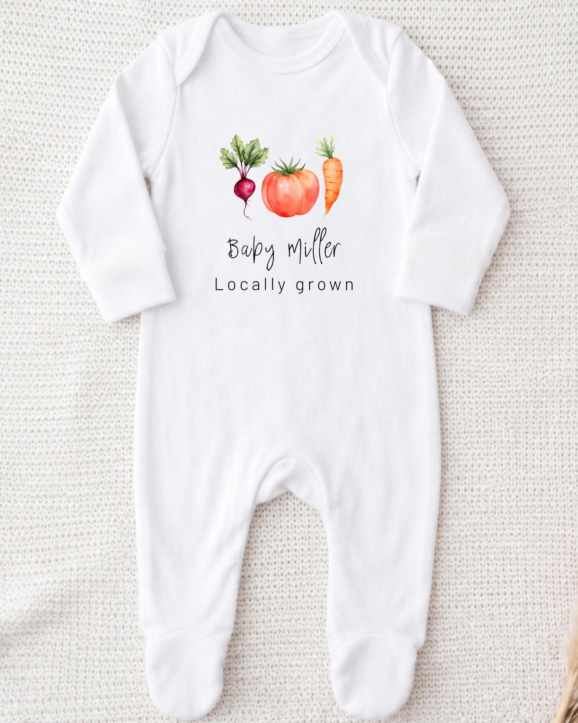 A white onesie with a graphic design of a carrot, tomato, and radish, along with the text "Baby Miller Locally grown".