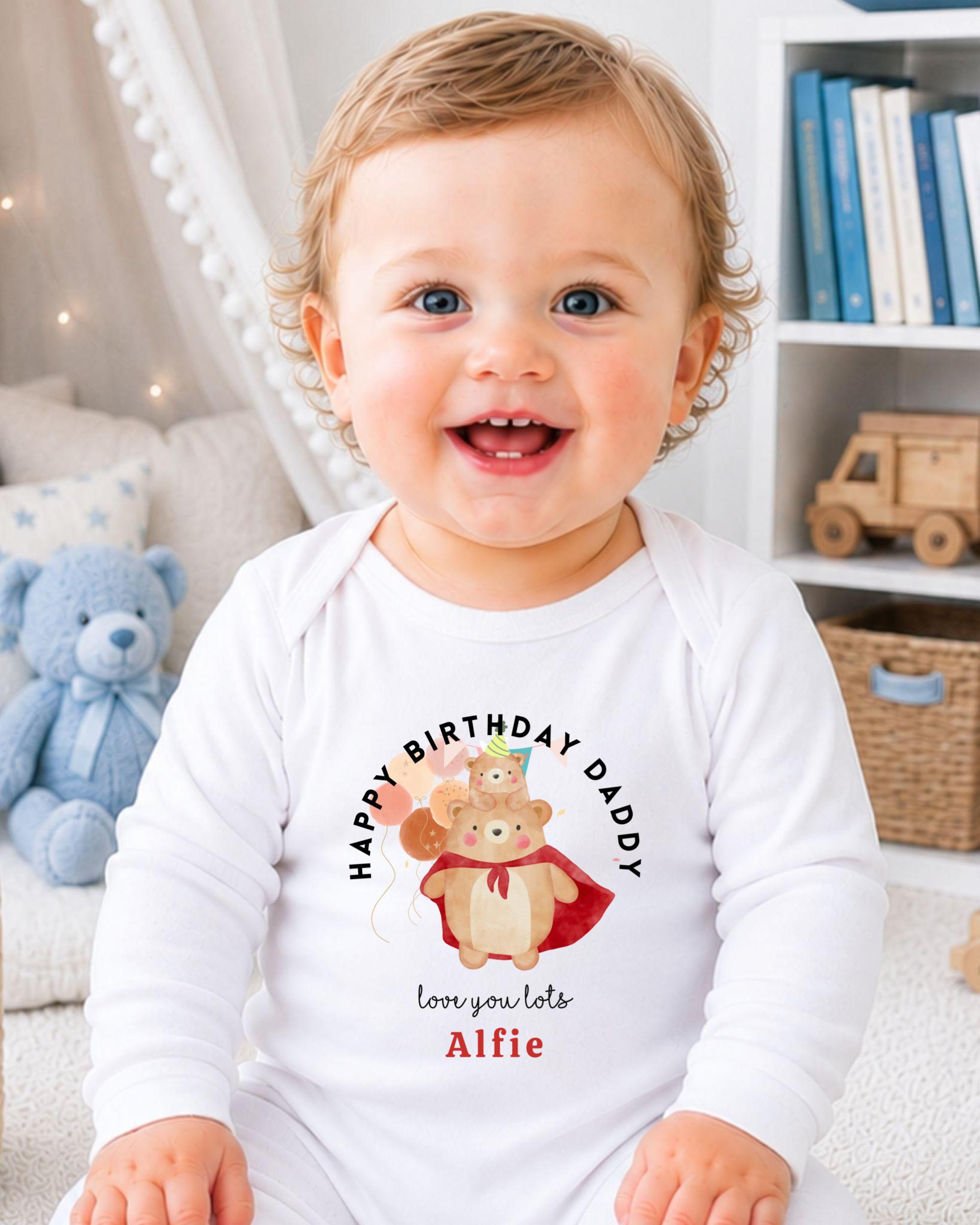 A smiling baby wearing a white onesie with a birthday message and a cartoon bear.
