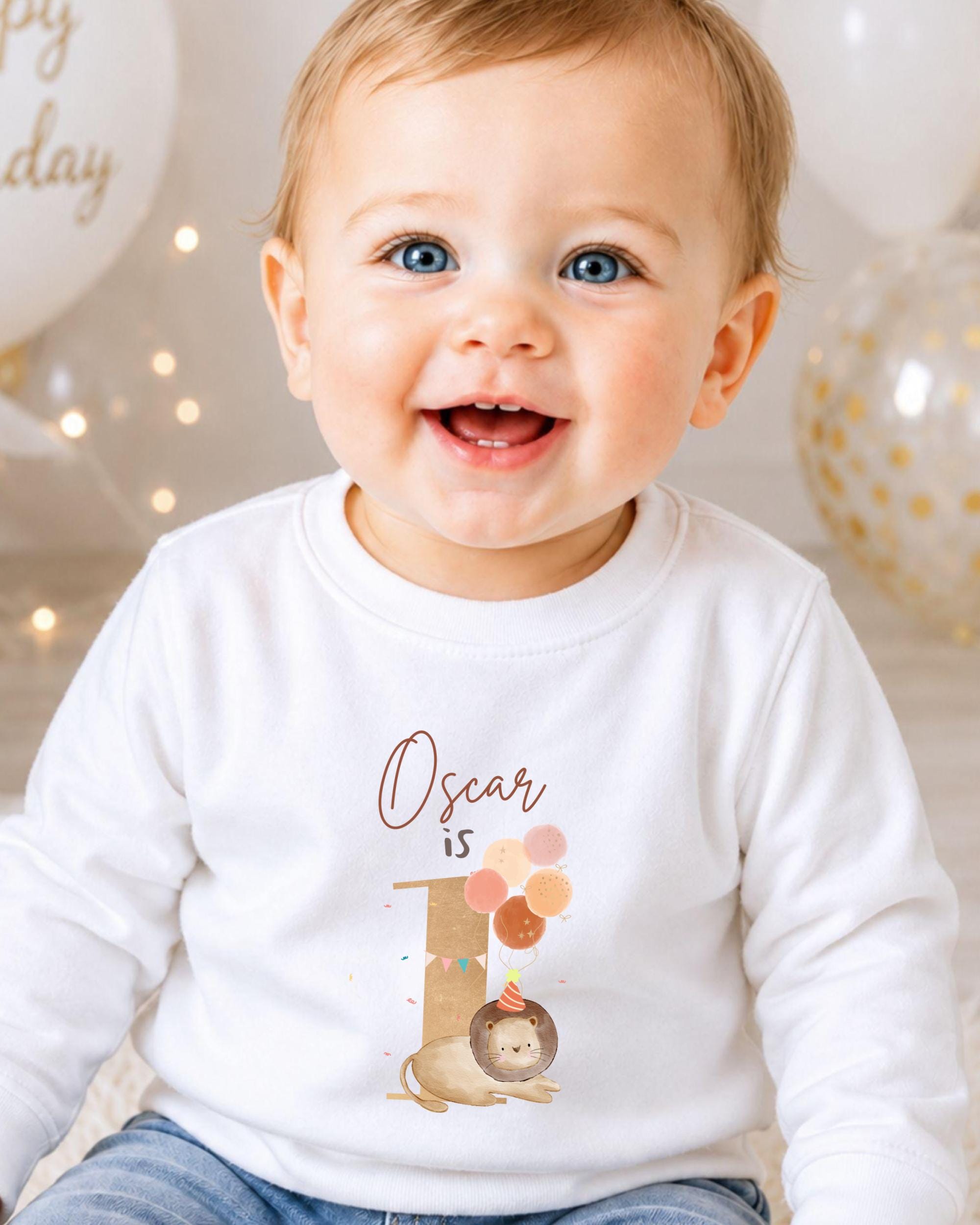 A smiling baby boy wearing a white shirt with a personalized birthday message and a sloth graphic.