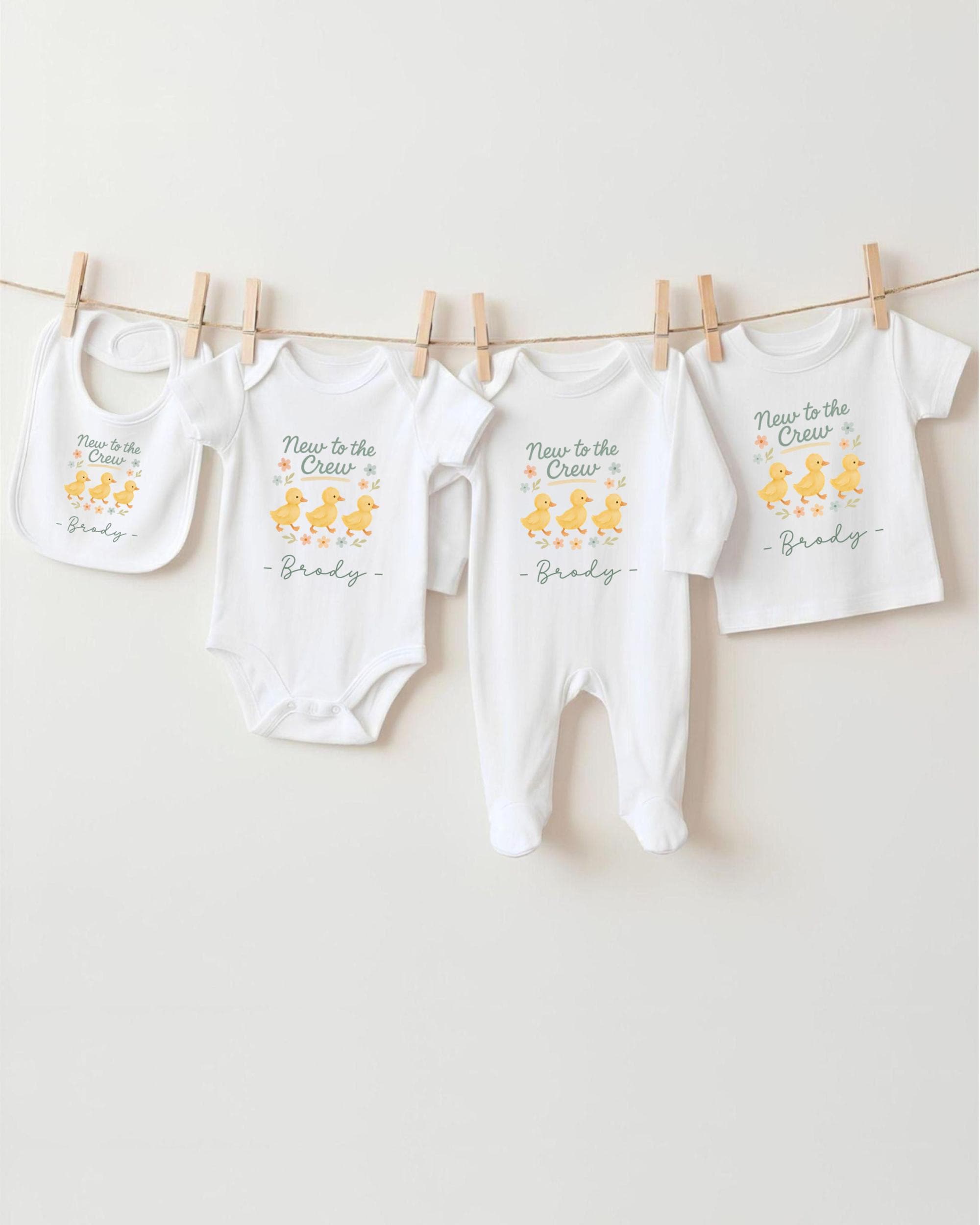 A row of baby clothes, including onesies and bibs, hanging on a clothesline.