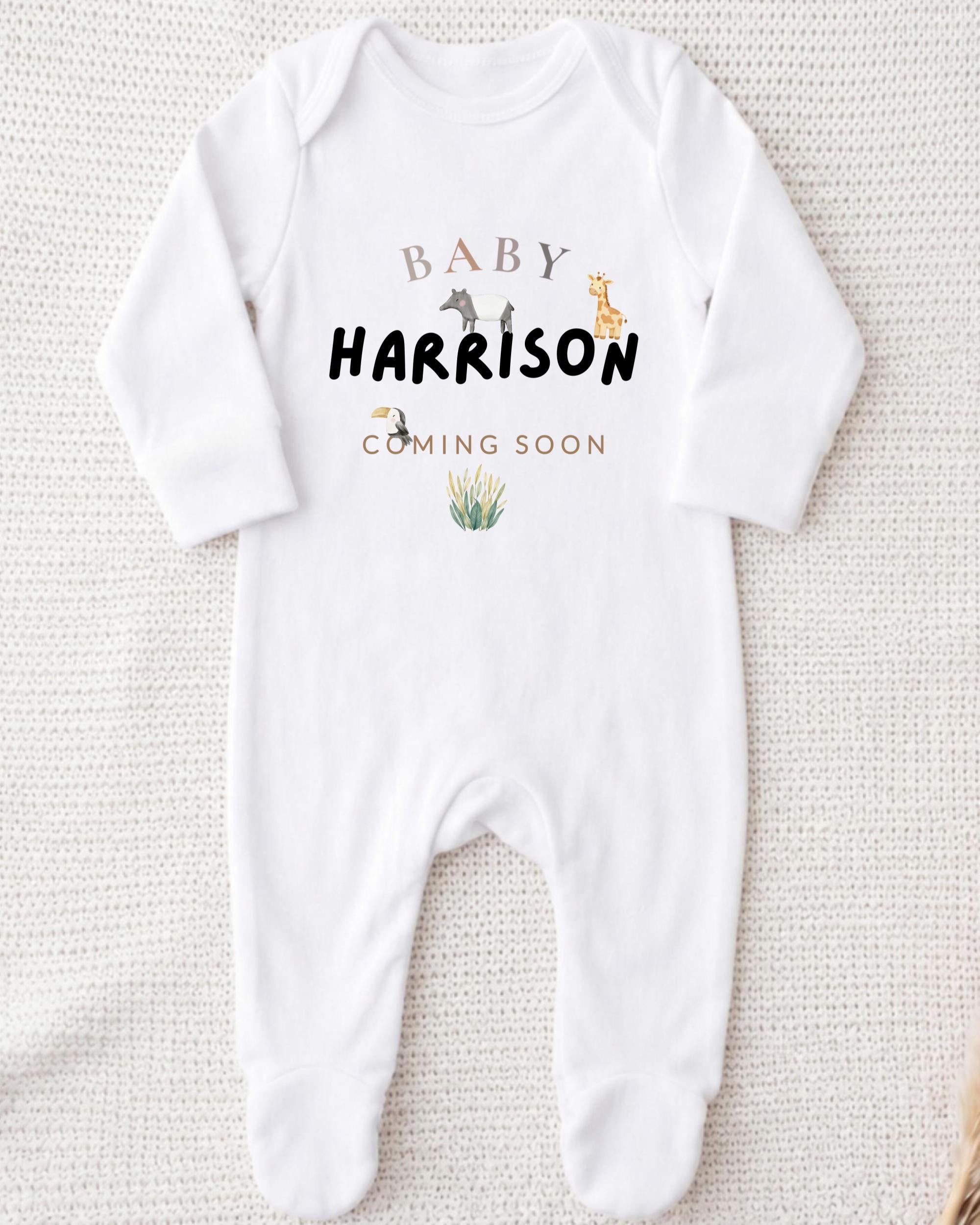 A white onesie with the text "BABY HARRISON COMING SOON" printed on it.
