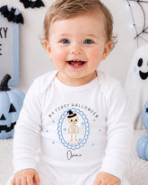 A smiling baby boy wearing a white onesie with a Halloween-themed design, including a skeleton and the text "My first Halloween Oscar".