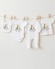 A row of four white baby clothes with a dinosaur design, hanging on a clothesline.