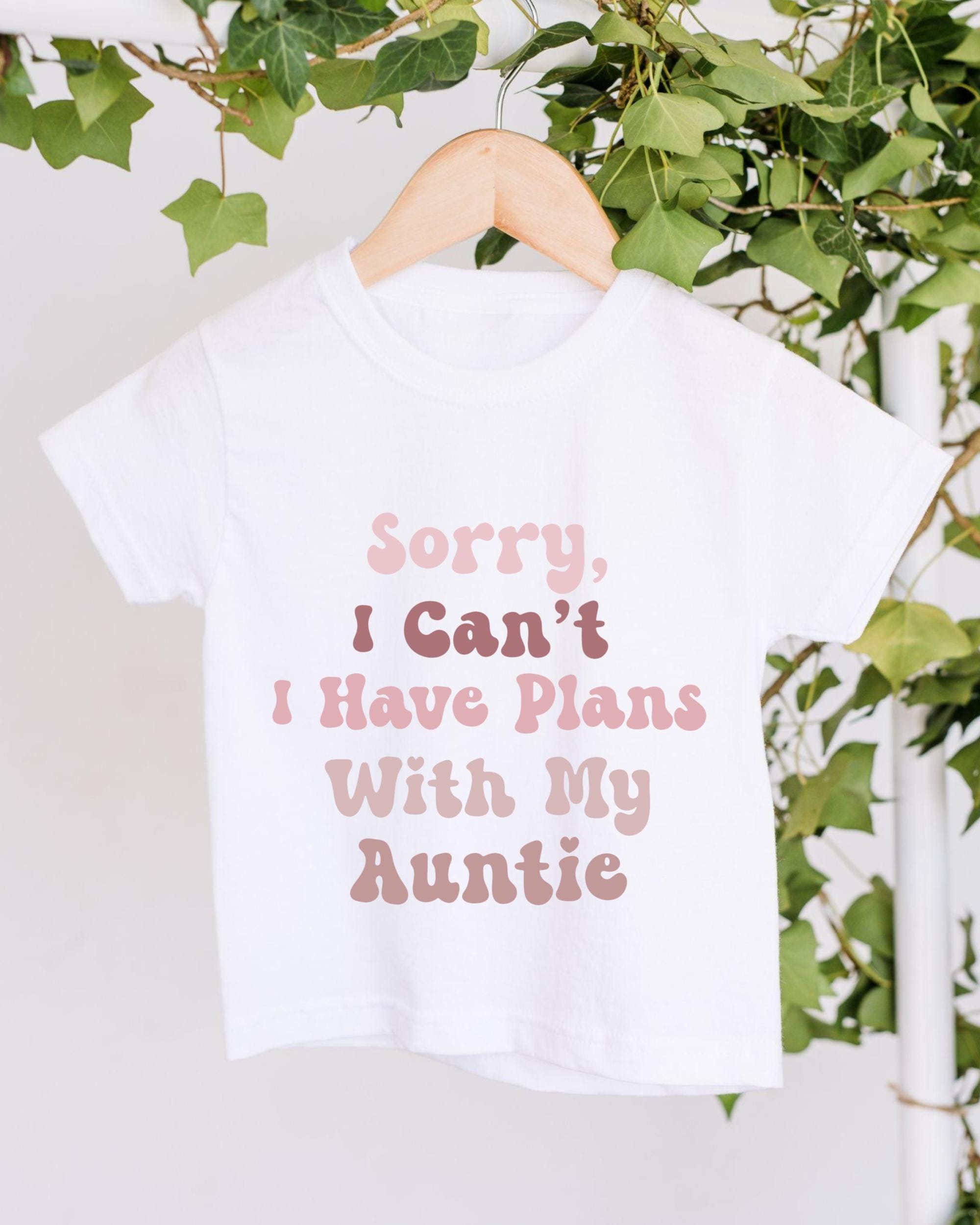 A white t-shirt with text printed on it, hanging on a wooden hanger.
