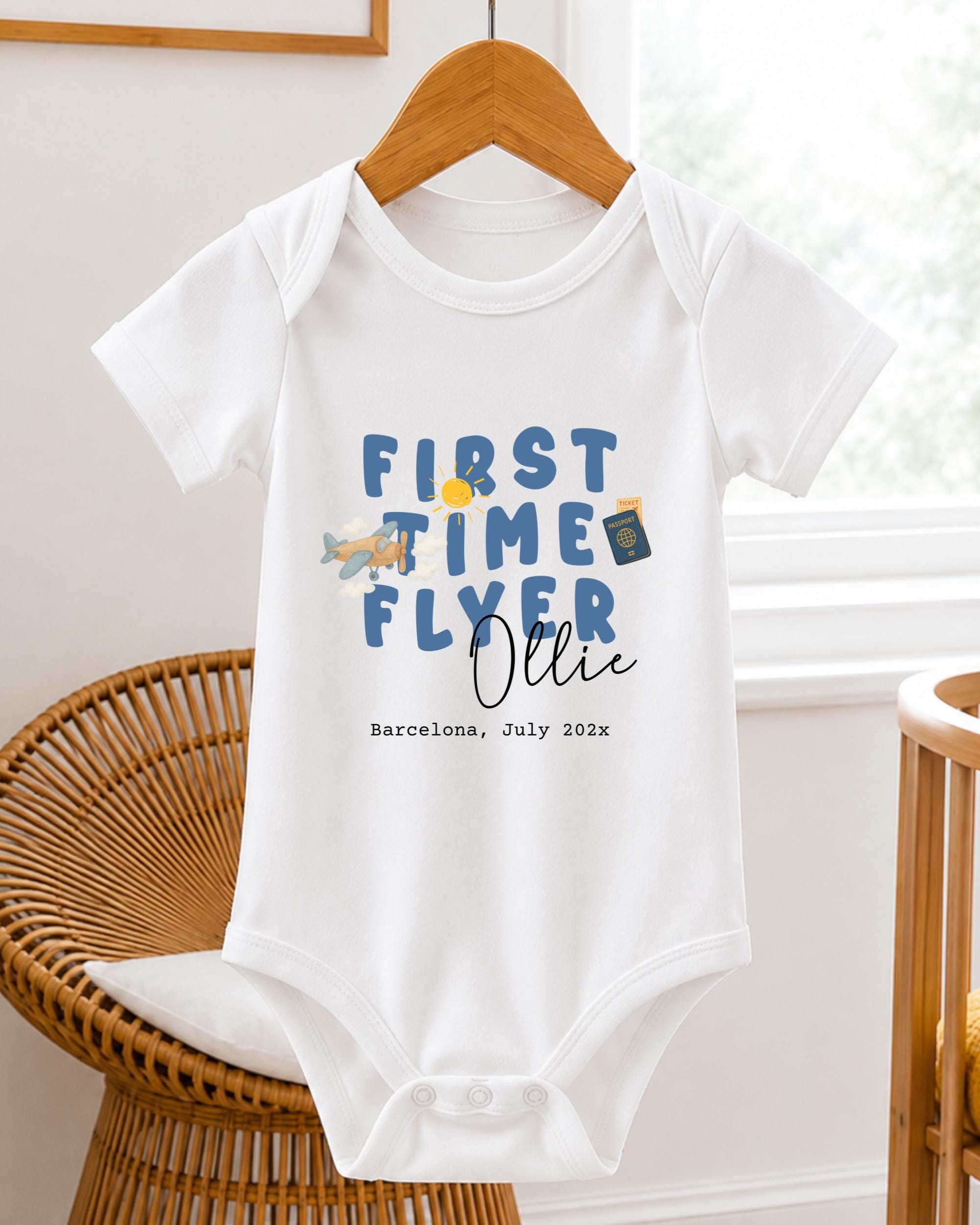 A white baby onesie with blue text and illustrations, hanging on a wooden hanger.