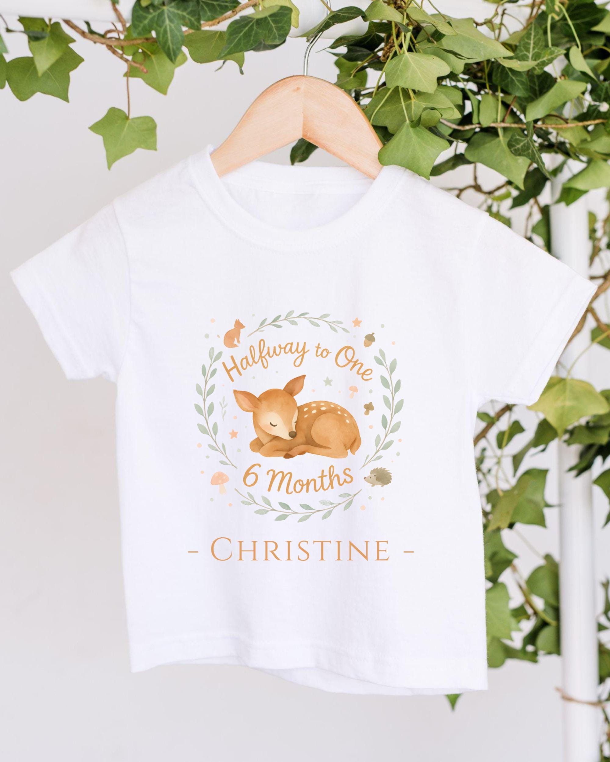 A white t-shirt with a graphic design featuring a sleeping deer and the text "Halfway to One 6 Months - Christine".