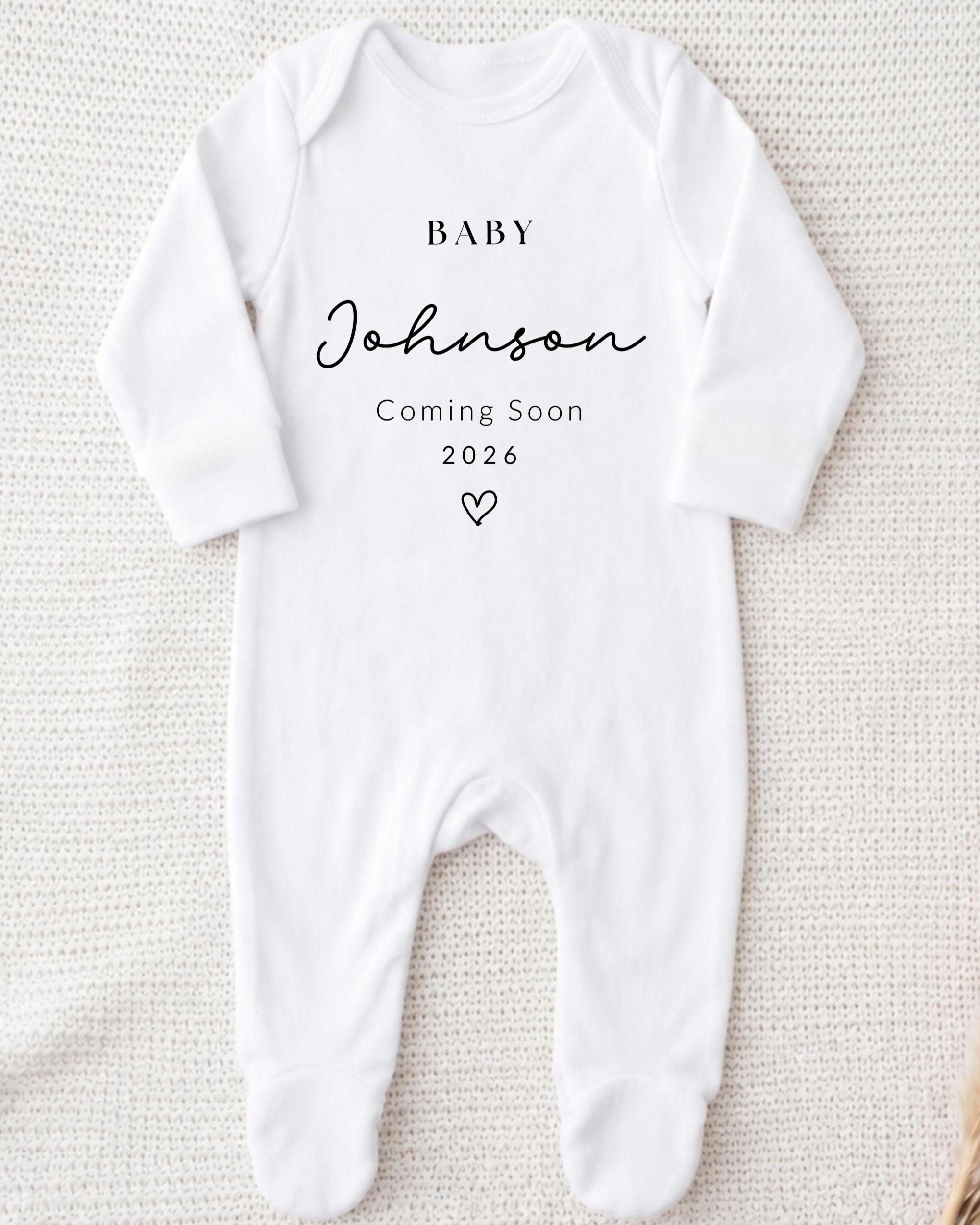 A white onesie with text printed on it, indicating that a baby named Johnson is coming soon.