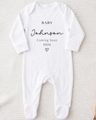 A white onesie with text printed on it, indicating that a baby named Johnson is coming soon.