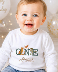 A smiling baby boy wearing a white shirt with a personalized name and animal print.