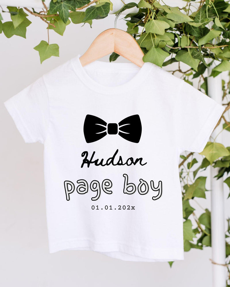 A white t-shirt with a black bow tie and text printed on it, hanging on a wooden hanger.