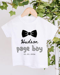 A white t-shirt with a black bow tie and text printed on it, hanging on a wooden hanger.