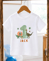 A white t-shirt with a dinosaur-themed design and the name "Jack" printed on it, hanging on a wooden hanger.