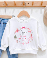 A white sweater with a personalized design hanging on a wooden hanger.
